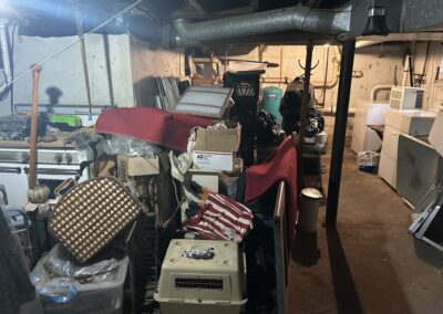 Cluttered basement utility room with a washer and dryer, exposed pipes, and piles of boxes and furniture.