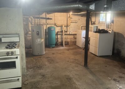 Basement utility room with a stove, water heater, and a washer/dryer set, exposed pipes, and a concrete floor.